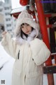 A woman in a white coat and hat standing in the snow.