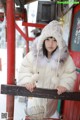 A woman in a white coat and hat leaning against a red pole.