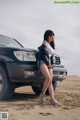 A woman standing next to a car in the desert.