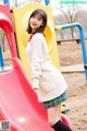 A young woman standing in front of a playground slide.