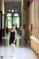 A young ballerina in a black leotard and white tights standing in a hallway.