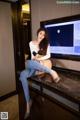 A woman sitting on top of a dresser in front of a television.