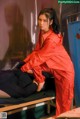 A woman in a red jumpsuit sitting on a bed.