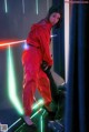 A woman in a red jumpsuit standing in front of a neon light.