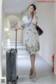 A woman in a cheongsam talking on a cell phone while holding a suitcase.