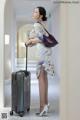 A woman in a cheongsam with a suitcase in a hallway.