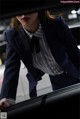 A woman in a business suit leaning against a car.