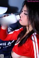 A woman in a red and white cheerleading uniform drinking from a bottle.