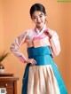 A woman in a pink and blue hanbok poses for a picture.