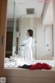 A woman in a white robe standing in a bathroom.