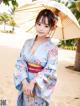 A woman in a blue kimono holding an umbrella on the beach.