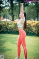 A woman in a white top and orange leggings stretching in a park.