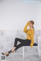 a woman sitting on a chair wearing a yellow sweater and black pants