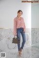 a woman wearing a pink blouse and jeans standing in front of a wall