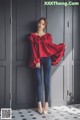 A woman standing in front of a gray wall wearing a red blouse.