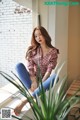 A woman sitting on a window sill next to a plant.