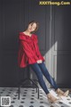 A woman sitting on a stool wearing a red blouse and jeans.