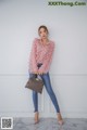 a woman standing in front of a white wall holding a brown bag