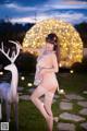 A woman in a white lingerie standing next to a white deer.