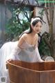 A woman in a white dress sitting in a wooden tub.