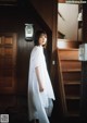 A woman in a white dress standing in front of a staircase.