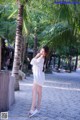 A woman in a white dress standing next to a palm tree.