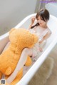 A woman sitting in a bathtub with a large teddy bear.