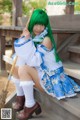 A woman with green hair sitting on a wooden bench holding a broom.