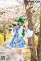 A woman in a blue and white dress standing next to a tree.