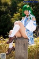 A woman with green hair sitting on a stone pillar.