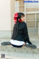 A woman sitting on the steps of a building wearing a black jacket and white skirt.