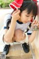 A young woman in a red and white outfit is drinking water from a faucet.