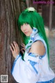 A woman with green hair leaning against a tree.