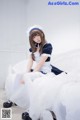 A woman in a maid outfit sitting on a bed.