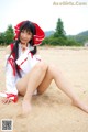 A woman in a red and white dress sitting on a beach.