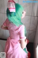 A woman in a pink dress with green hair and a pink bow.