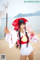 A woman in a white bathing suit holding a red and white umbrella.