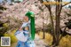 A woman with green hair standing in front of cherry blossoms.