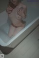 A naked woman sitting in a bathtub with a tattoo on her arm.