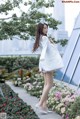 A woman in a white coat standing in a flower garden.