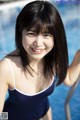 A woman in a blue bathing suit posing by a swimming pool.