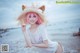 A woman with pink hair wearing a straw hat on the beach.