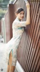 A woman in a blue and white dress leaning against a fence.