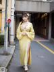 A woman in a yellow kimono is walking down the street.