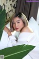 A woman laying on top of a bed next to a green leaf.