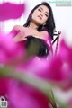 A woman in a black dress sitting on a chair surrounded by pink flowers.