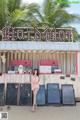 A woman standing in front of a food stand on the beach.