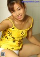 A woman in a yellow tank top sitting on a toilet.