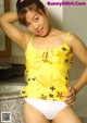 A woman in a yellow top and white panties posing in a bathroom.