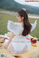 A woman in a white dress sitting on a picnic blanket.